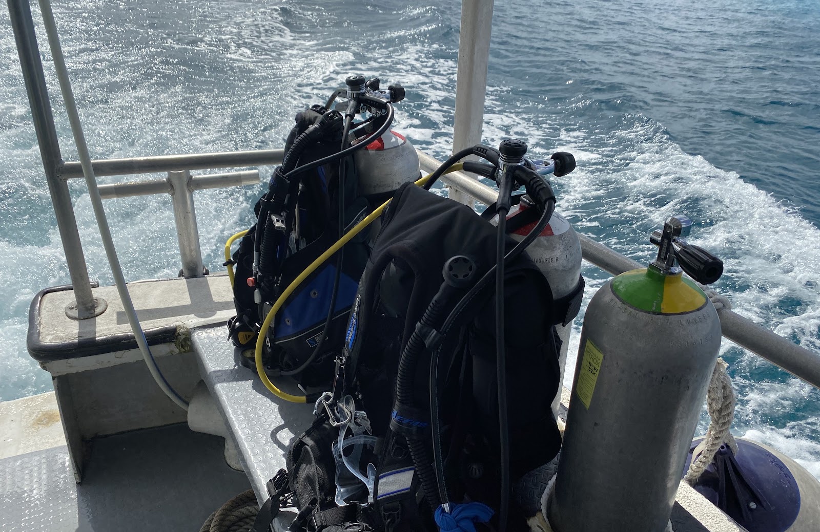 Dive gear and a nitrox marked tank stowed on the rail as the boat runs out over open water